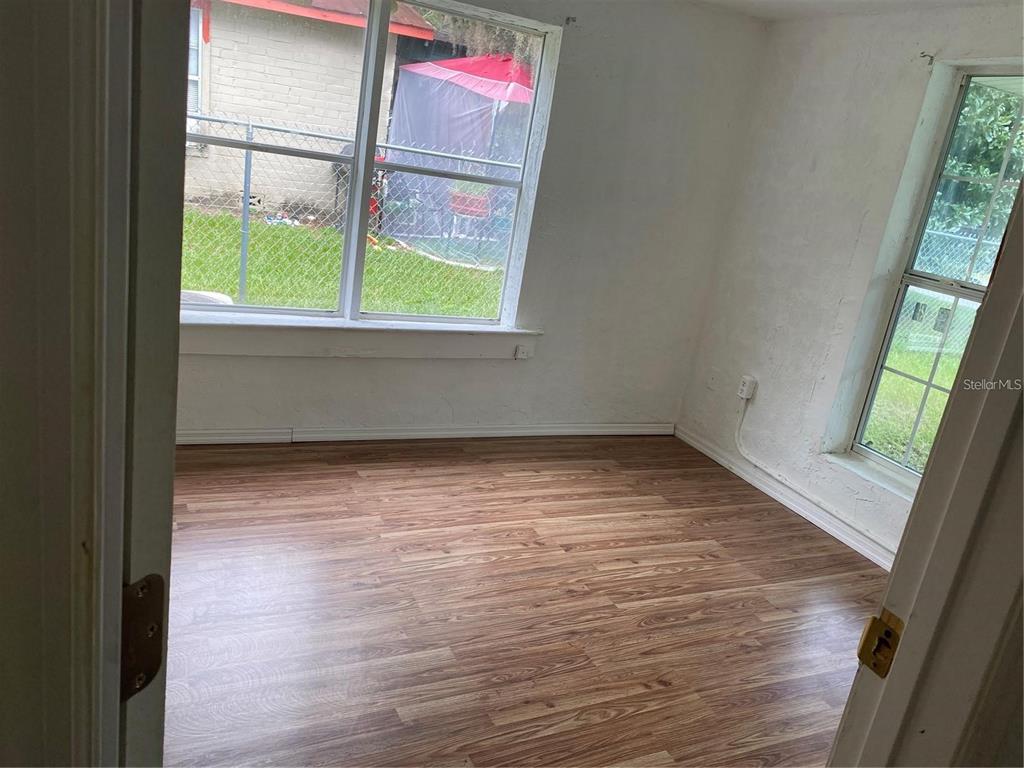 An empty room features wood-look laminate flooring, white walls, and two windows overlooking a yard — 414 NW 9TH AVENUE, OCALA, FL