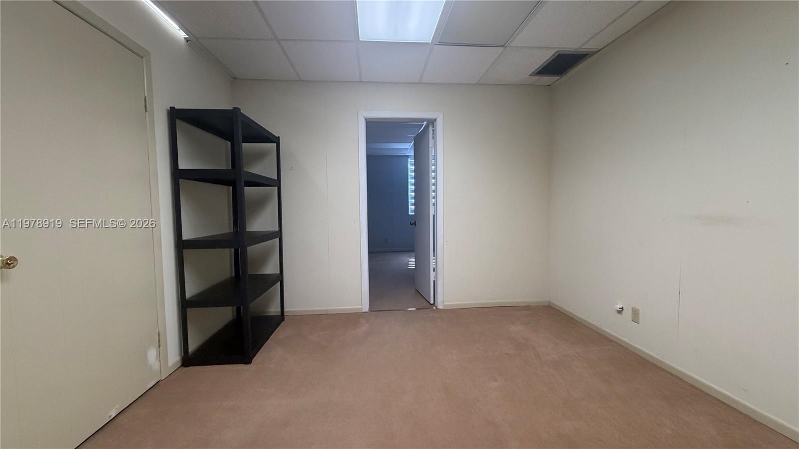 A small, empty office room features beige carpet, white walls, a black shelf, and a doorway — 2435 Hollywood Blvd, Hollywood FL 33020, HOLLYWOOD, FL