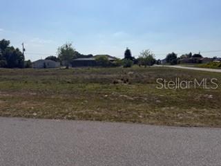 A vacant, grassy residential lot sits along a paved road under a clear blue sky — 2993 SEAFARER DRIVE, PUNTA GORDA, FL