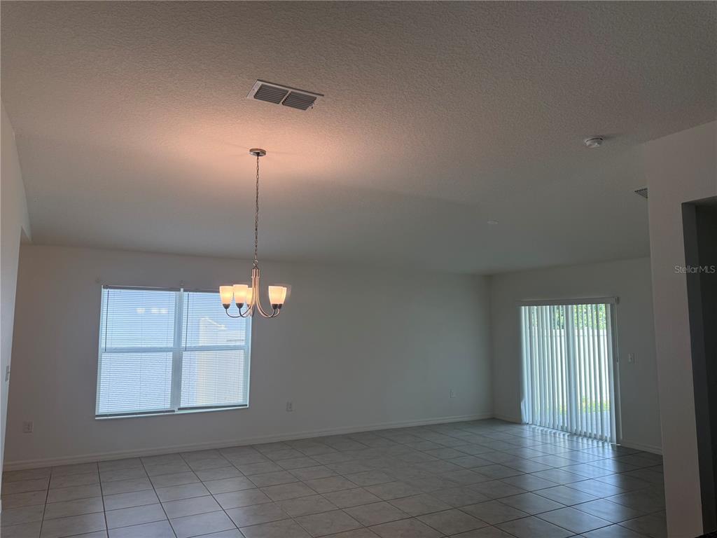 An empty dining area features tile flooring, a chandelier, a window, and sliding glass doors — 711 SCRUB OAK HAMMOCK ROAD, DAVENPORT, FL