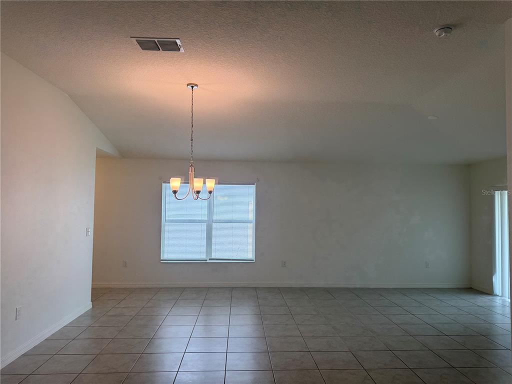 An empty dining area features tile flooring, a chandelier, and a large window — 711 SCRUB OAK HAMMOCK ROAD, DAVENPORT, FL