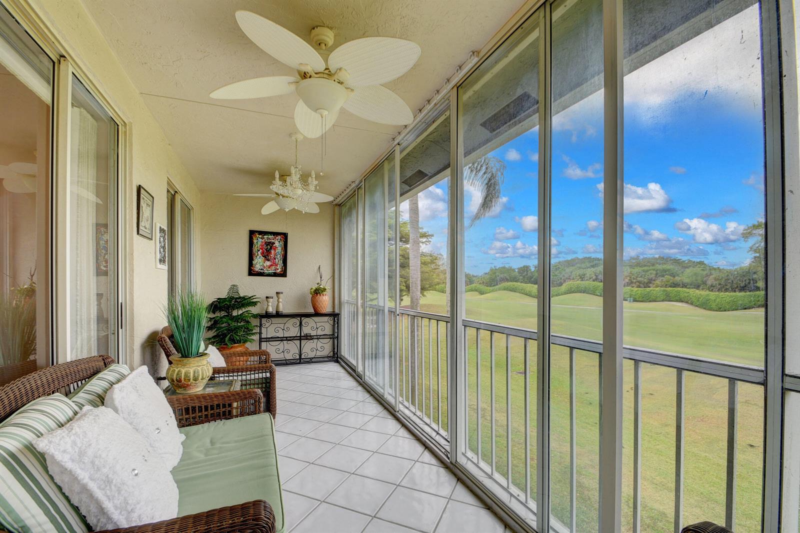 A screened-in balcony with tile flooring, wicker furniture, and a view of a golf course — 10220 Andover Coach Circle # H2, Lake Worth FL 33449, LAKE WORTH, FL