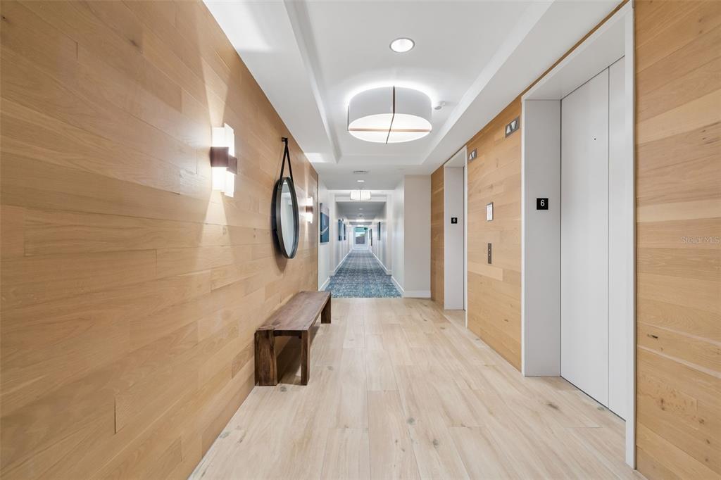 A hallway features light wood-paneled walls, a wooden bench, a mirror, and elevator doors — 920 N OSCEOLA AVENUE UNIT 604, CLEARWATER, FL