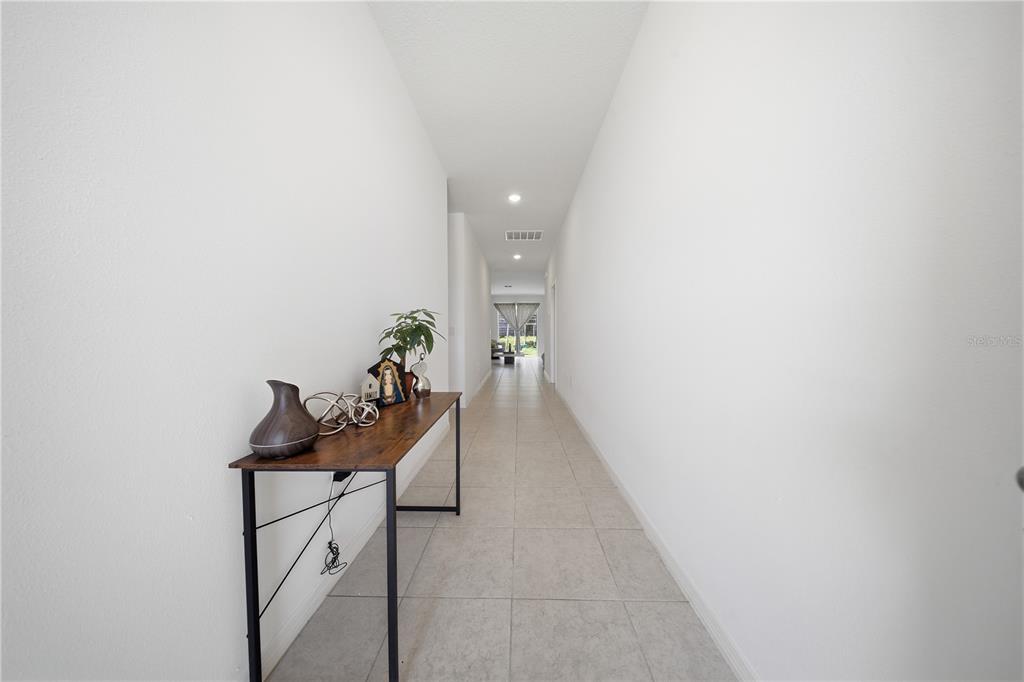 A long hallway with white walls, tile flooring, and a narrow wooden console table — 788 RICHMOND ESTATE AVENUE, HAINES CITY, FL