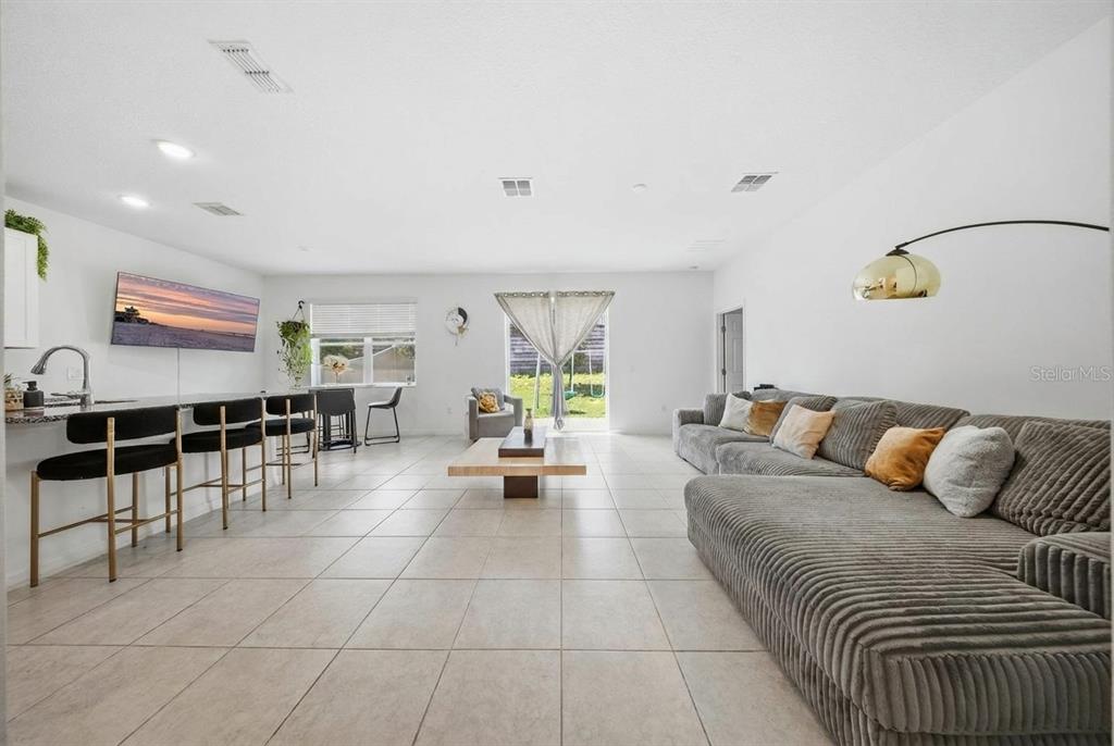 A spacious open-concept living room features tile flooring, a large sectional sofa, and a kitchen island — 788 RICHMOND ESTATE AVENUE, HAINES CITY, FL