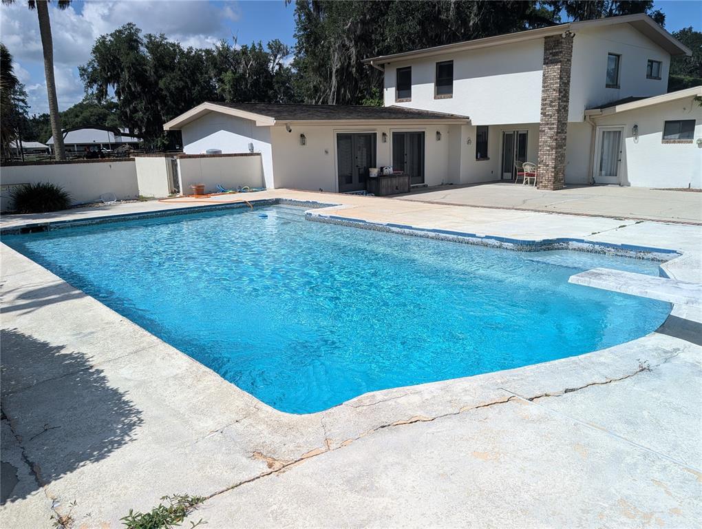 A rectangular swimming pool sits on a concrete patio in front of a two-story house — 1750 SE 80TH STREET, OCALA, FL