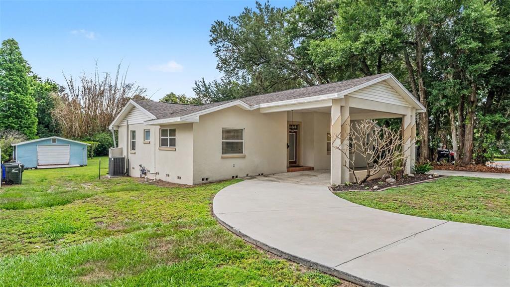 A light-colored single-story house with a carport and a detached shed in the yard — 926 HOLLINGSWORTH ROAD, LAKELAND, FL