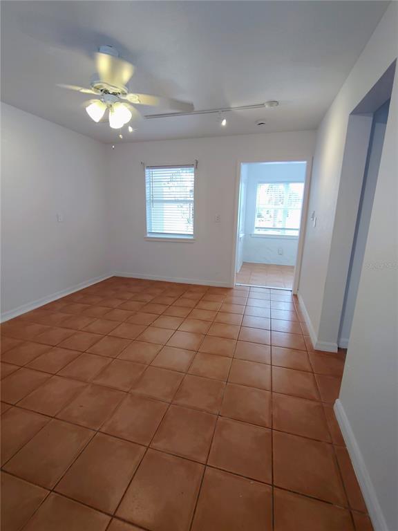 An empty room with terracotta tile flooring, a ceiling fan, and a doorway to another room — 115 145TH AVENUE E UNIT 6, MADEIRA BEACH, FL