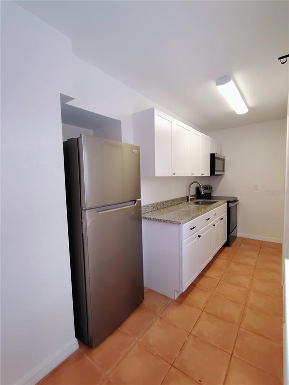A kitchen features white cabinets, granite countertops, stainless steel appliances, and terracotta tile flooring — 115 145TH AVENUE E UNIT 6, MADEIRA BEACH, FL