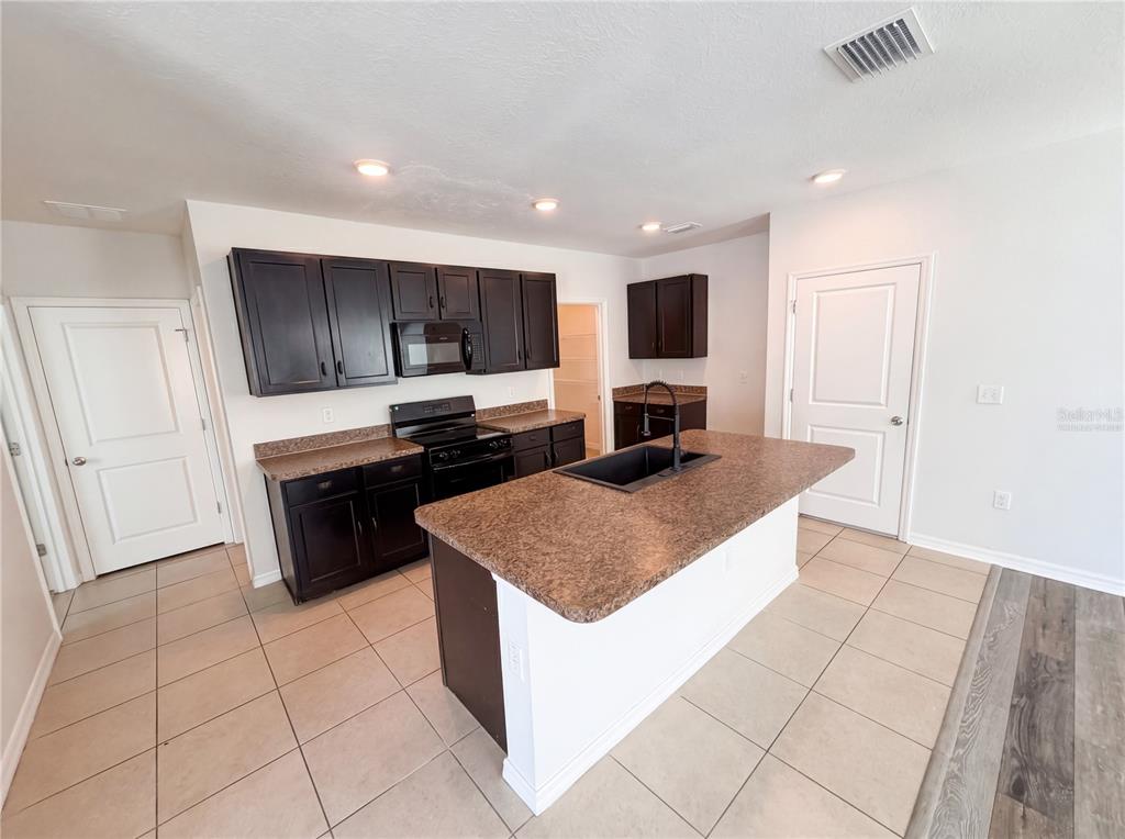 A kitchen features dark wood cabinets, brown laminate countertops, a center island, and tile flooring — 10225 MANGROVE WELL ROAD, SUN CITY CENTER, FL