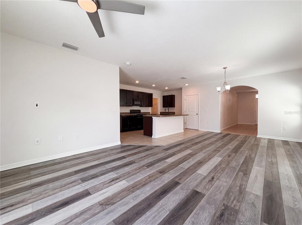 An open-concept living area features wood-look flooring, a ceiling fan, and an adjacent kitchen — 10225 MANGROVE WELL ROAD, SUN CITY CENTER, FL