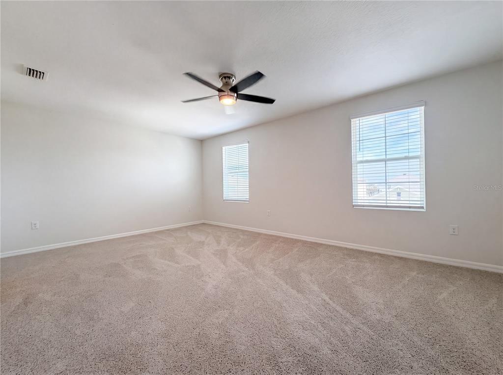 An empty bedroom features beige carpeting, white walls, a ceiling fan, and two windows — 10225 MANGROVE WELL ROAD, SUN CITY CENTER, FL