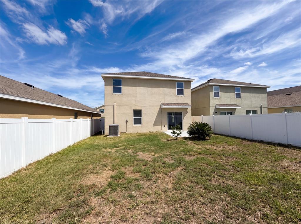 The rear exterior of a two-story house features a small patio and a fenced yard — 10225 MANGROVE WELL ROAD, SUN CITY CENTER, FL