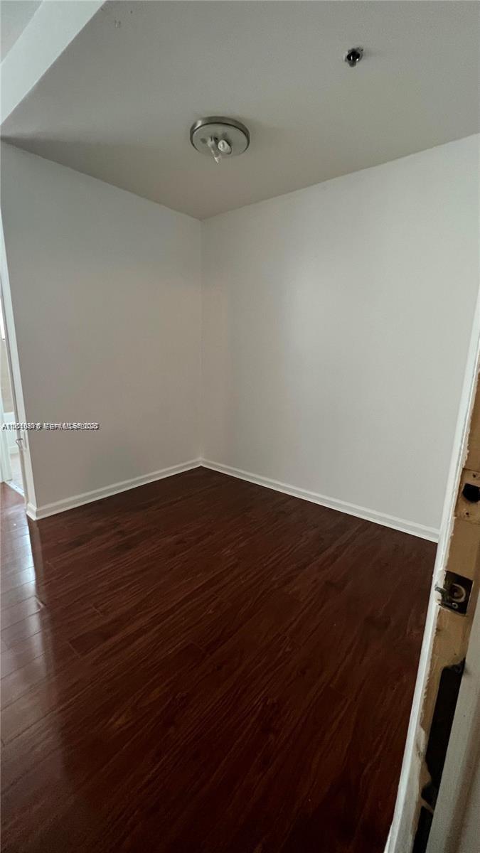 An empty room features white walls, dark wood-look flooring, and a ceiling-mounted light fixture — 1502 Jefferson Ave # 102, Miami Beach FL 33139, MIAMI BEACH, FL