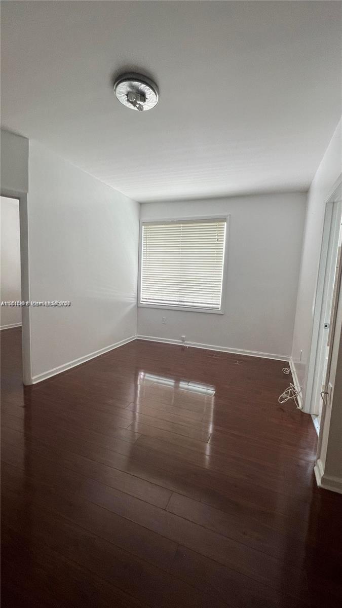 An empty room features dark wood-look flooring, white walls, and a window with blinds — 1502 Jefferson Ave # 102, Miami Beach FL 33139, MIAMI BEACH, FL