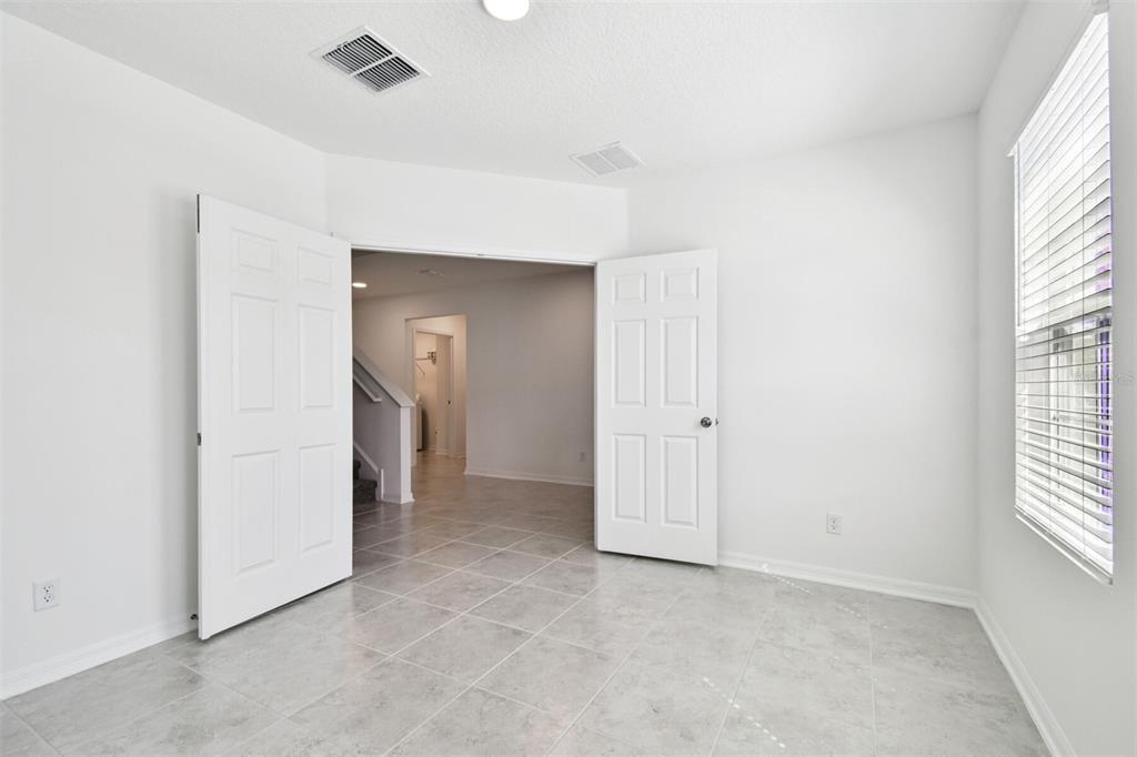 A room with light gray tile flooring, white walls, and double doors opening to a hallway — 12801 CASTLE OAKS DRIVE, HUDSON, FL