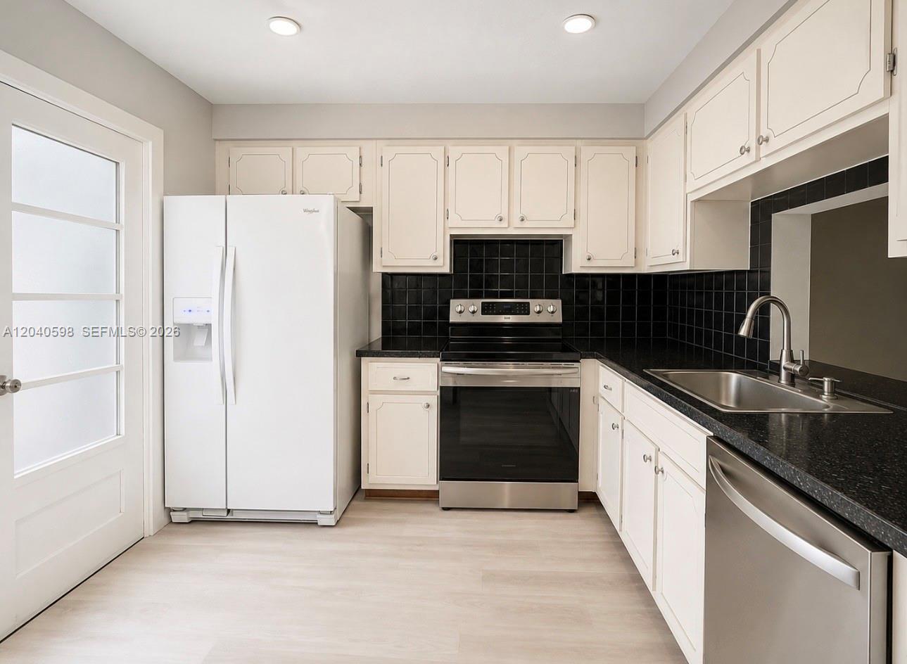 A kitchen features white cabinets, black tile backsplashes, black countertops, and stainless steel appliances — 1893 S Ocean Dr # 601, Hallandale Beach FL 33009, HALLANDALE BEACH, FL