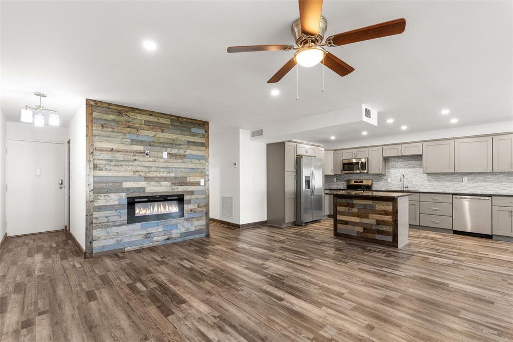 An open-concept living area features wood-plank flooring, a fireplace accent wall, and a modern kitchen — 225 COUNTRY CLUB DRIVE UNIT B221, LARGO, FL
