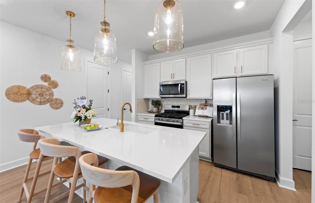 A modern kitchen features white cabinets, a quartz island with bar seating, and stainless appliances — 320 FISHTAIL PLACE, PALM COAST, FL