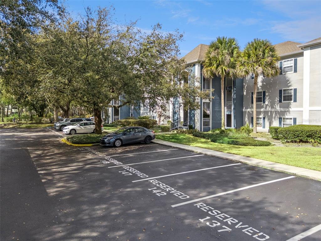 An apartment building exterior features a parking lot with numbered reserved spaces and palm trees — 8201 OLYMPIA COURT UNIT 8201, LONGWOOD, FL