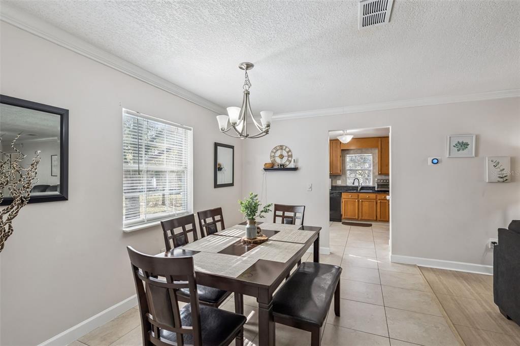 A dining room with a wooden table, chairs, bench, chandelier, and a view into the kitchen — 8201 OLYMPIA COURT UNIT 8201, LONGWOOD, FL