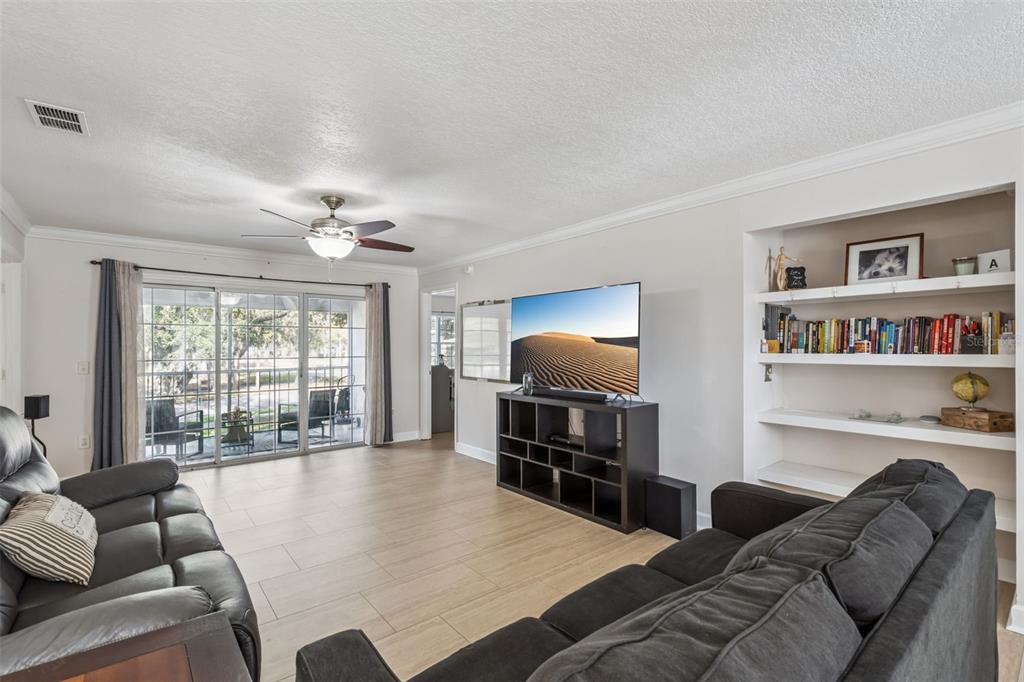 A living room features light tile flooring, a ceiling fan, a television, and built-in shelves — 8201 OLYMPIA COURT UNIT 8201, LONGWOOD, FL