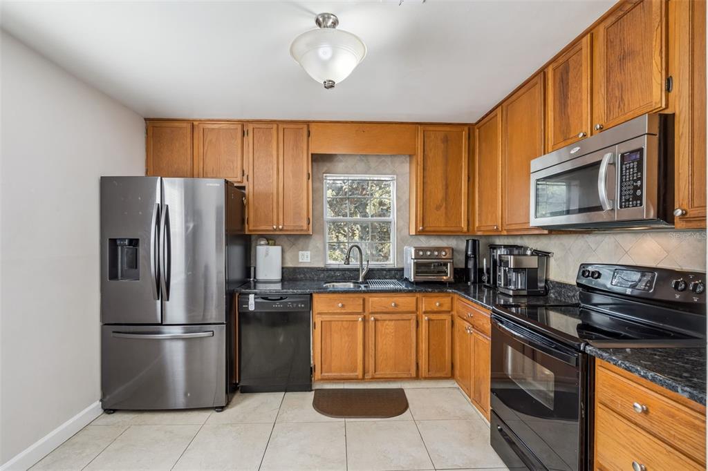 A kitchen features wood cabinets, stainless steel appliances, dark countertops, and light tile flooring — 8201 OLYMPIA COURT UNIT 8201, LONGWOOD, FL