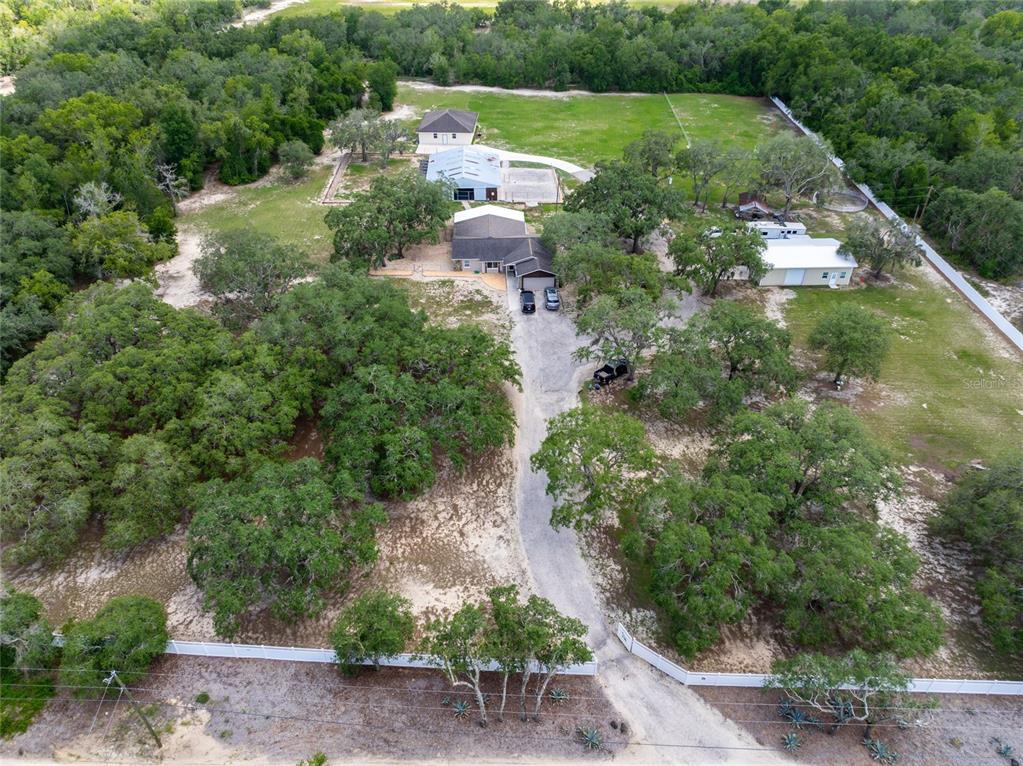 An aerial view shows a house, several outbuildings, and a gravel driveway on a wooded lot — 16142 BREAKWATER LANE, SPRING HILL, FL