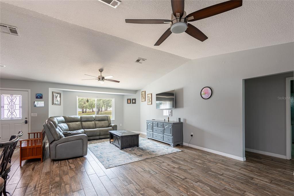 A living room features a gray sectional sofa, wood-look flooring, and a ceiling fan — 16142 BREAKWATER LANE, SPRING HILL, FL