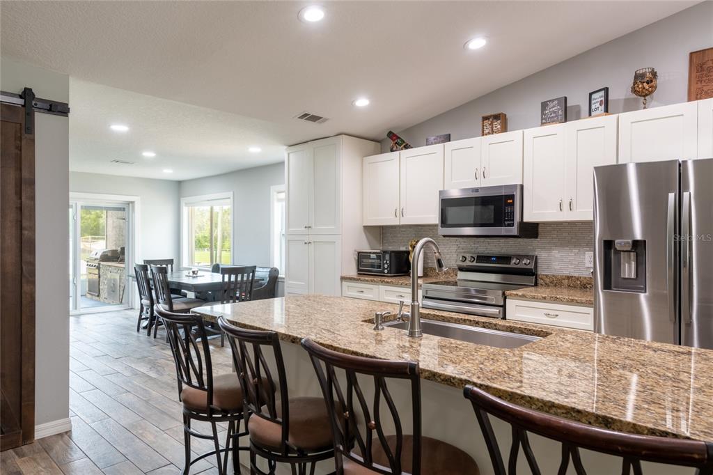A kitchen features white cabinets, granite countertops, a center island, and an adjacent dining area — 16142 BREAKWATER LANE, SPRING HILL, FL