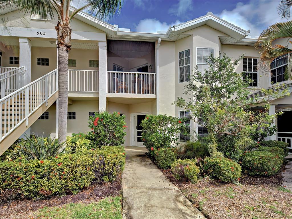A two-story residential building features a ground-level entrance, a screened balcony, and landscaped shrubbery — 902 ADDINGTON COURT UNIT 103, VENICE, FL