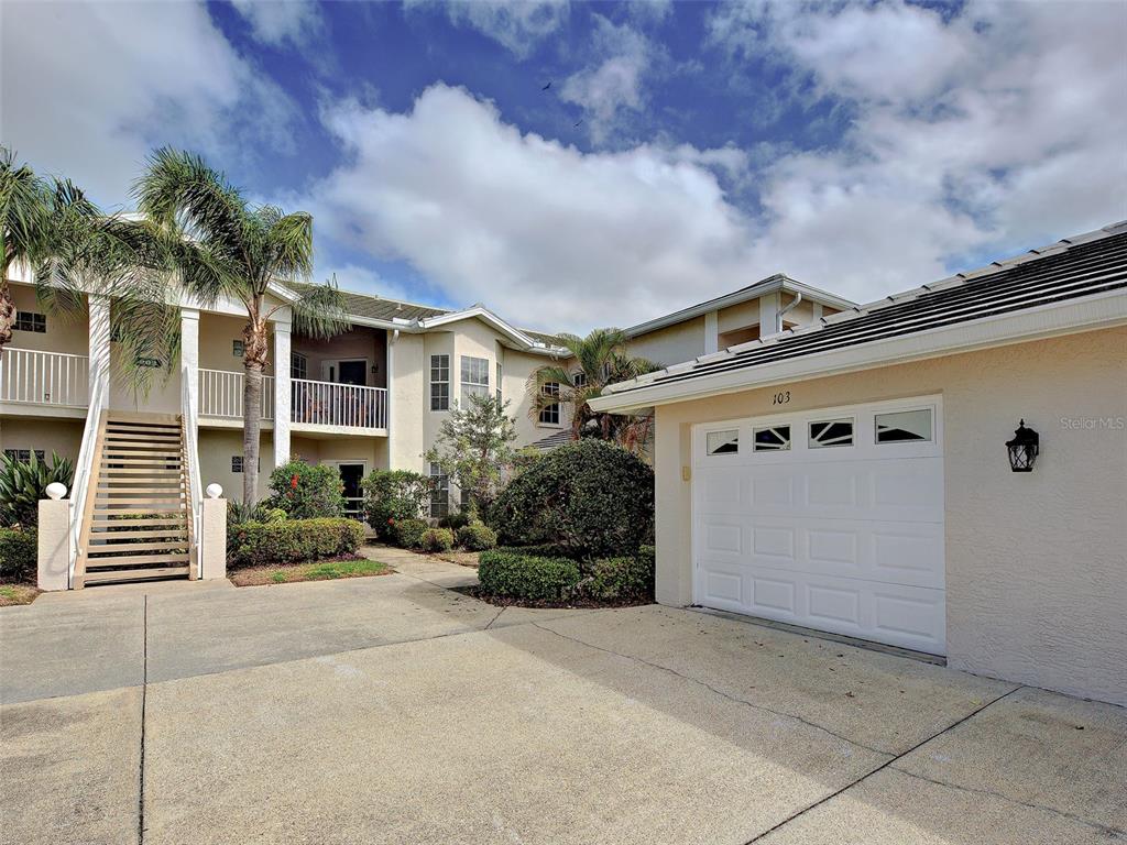 A two-story residential building with a white garage, a staircase, and palm trees — 902 ADDINGTON COURT UNIT 103, VENICE, FL