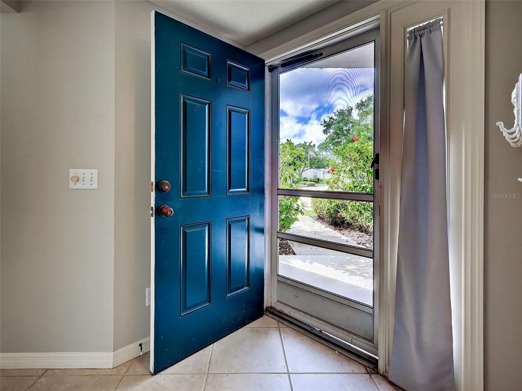 An open blue front door reveals a screen door and a view of outdoor landscaping — 902 ADDINGTON COURT UNIT 103, VENICE, FL