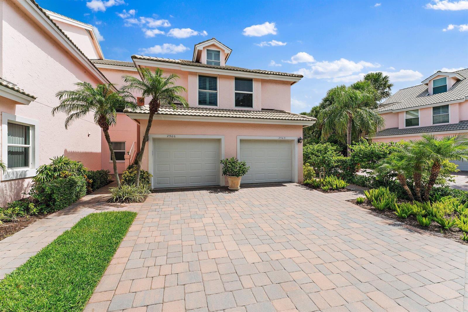 A two-story pink stucco townhouse features two garage doors and a paved driveway — 2905 Fairway Drive N, Jupiter FL 33477, JUPITER, FL