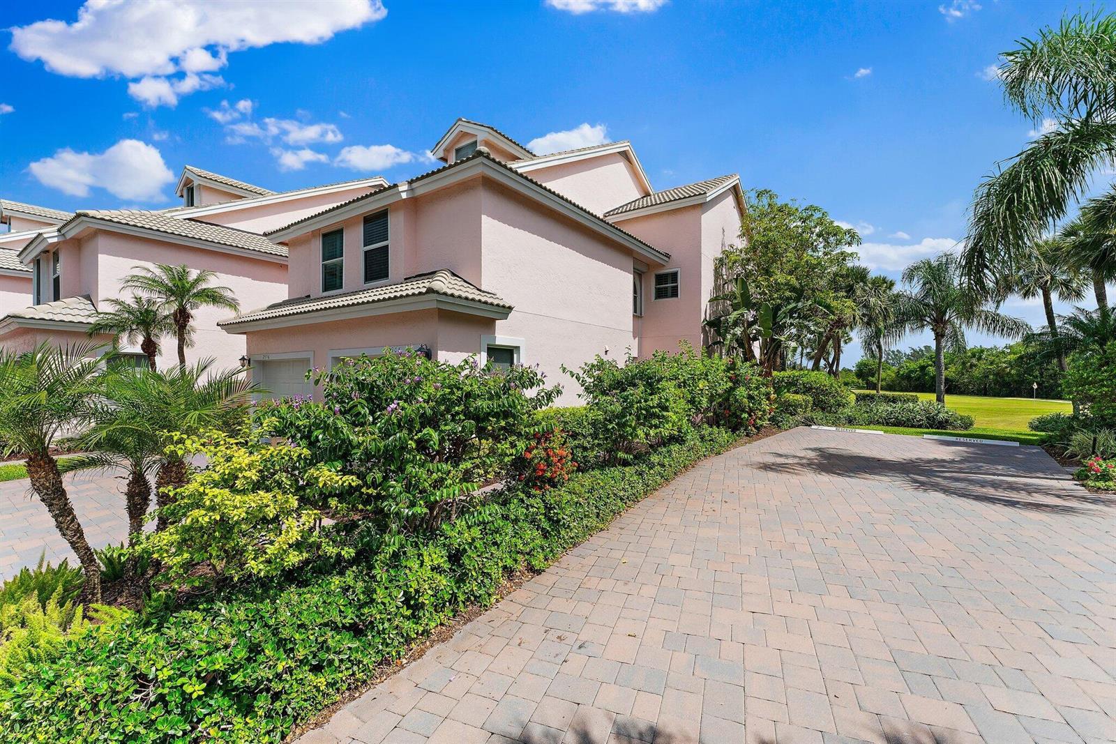 A light pink two-story townhouse features a paved driveway and lush landscaping under a blue sky — 2905 Fairway Drive N, Jupiter FL 33477, JUPITER, FL