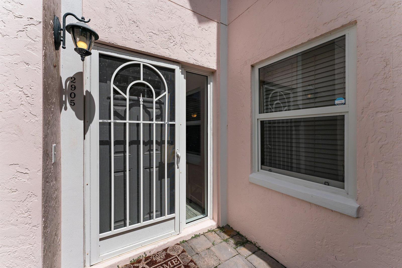 A pink stucco exterior features a white screen door, a window, and a wall-mounted light — 2905 Fairway Drive N, Jupiter FL 33477, JUPITER, FL