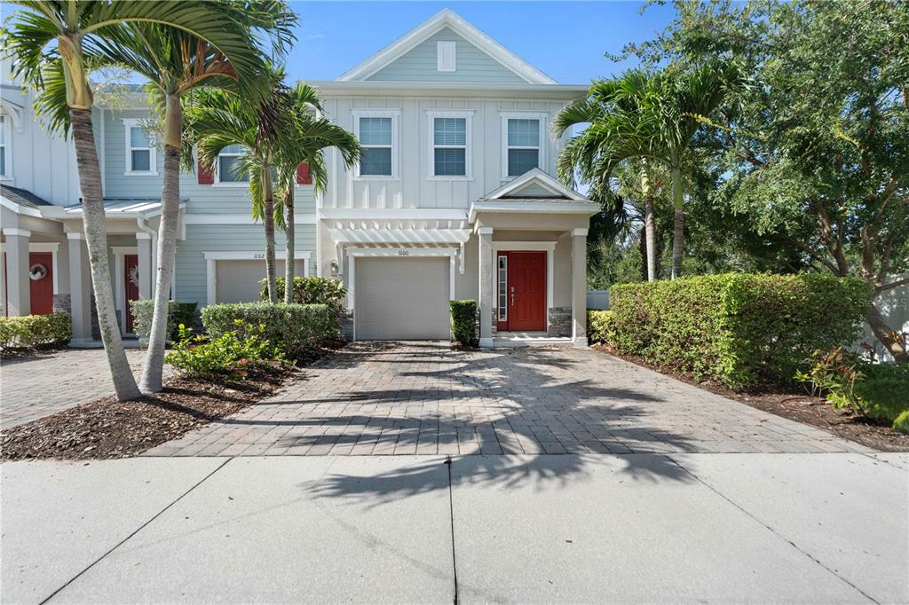 A two-story townhouse with a red front door, a garage, and a paved driveway — 1100 CORAL LANE, DUNEDIN, FL
