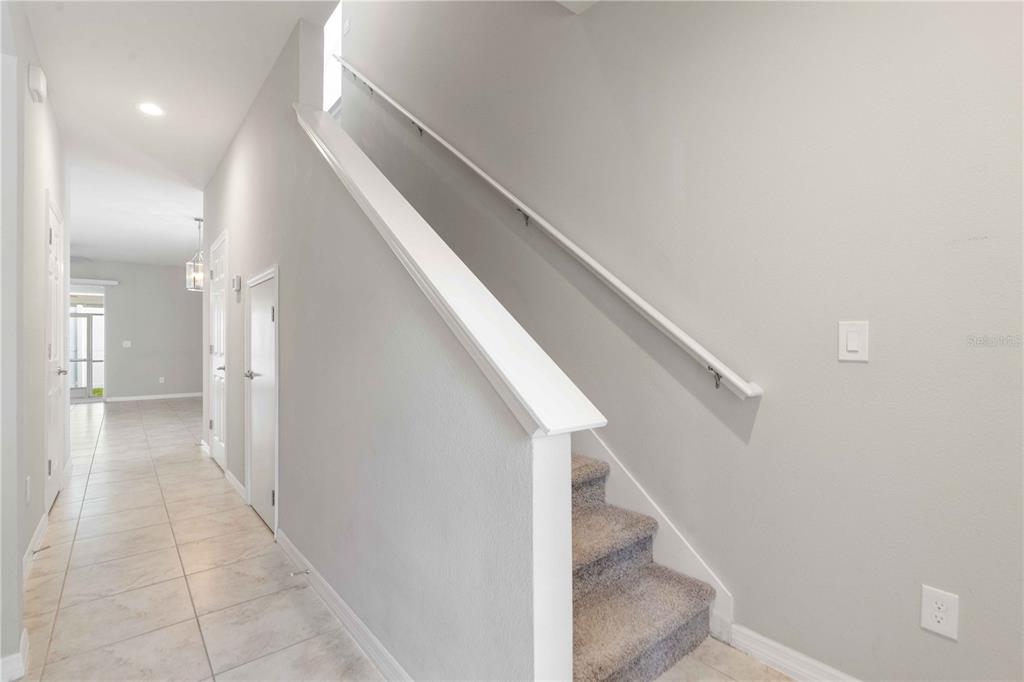 A hallway with light tile flooring leads to a carpeted staircase with a white railing — 1100 CORAL LANE, DUNEDIN, FL
