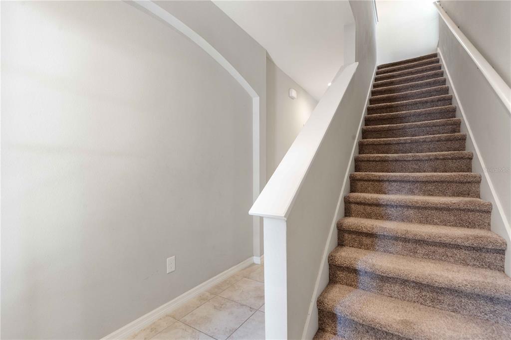 A carpeted staircase with a white railing leads upward next to a tiled entryway — 1100 CORAL LANE, DUNEDIN, FL