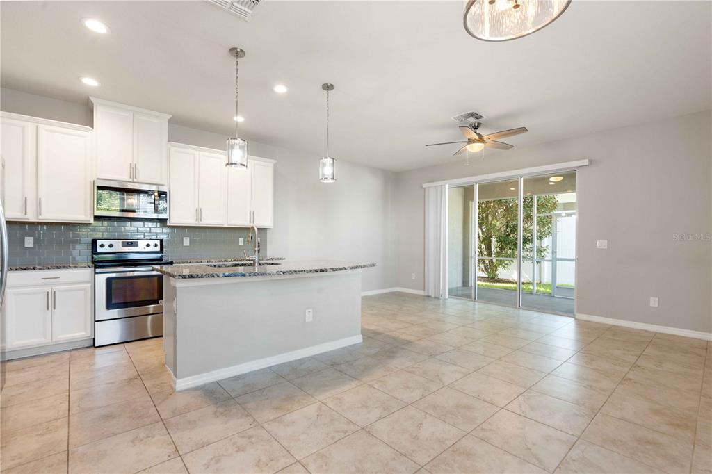A kitchen with white cabinets, stainless steel appliances, and a granite island opens to a patio — 1100 CORAL LANE, DUNEDIN, FL