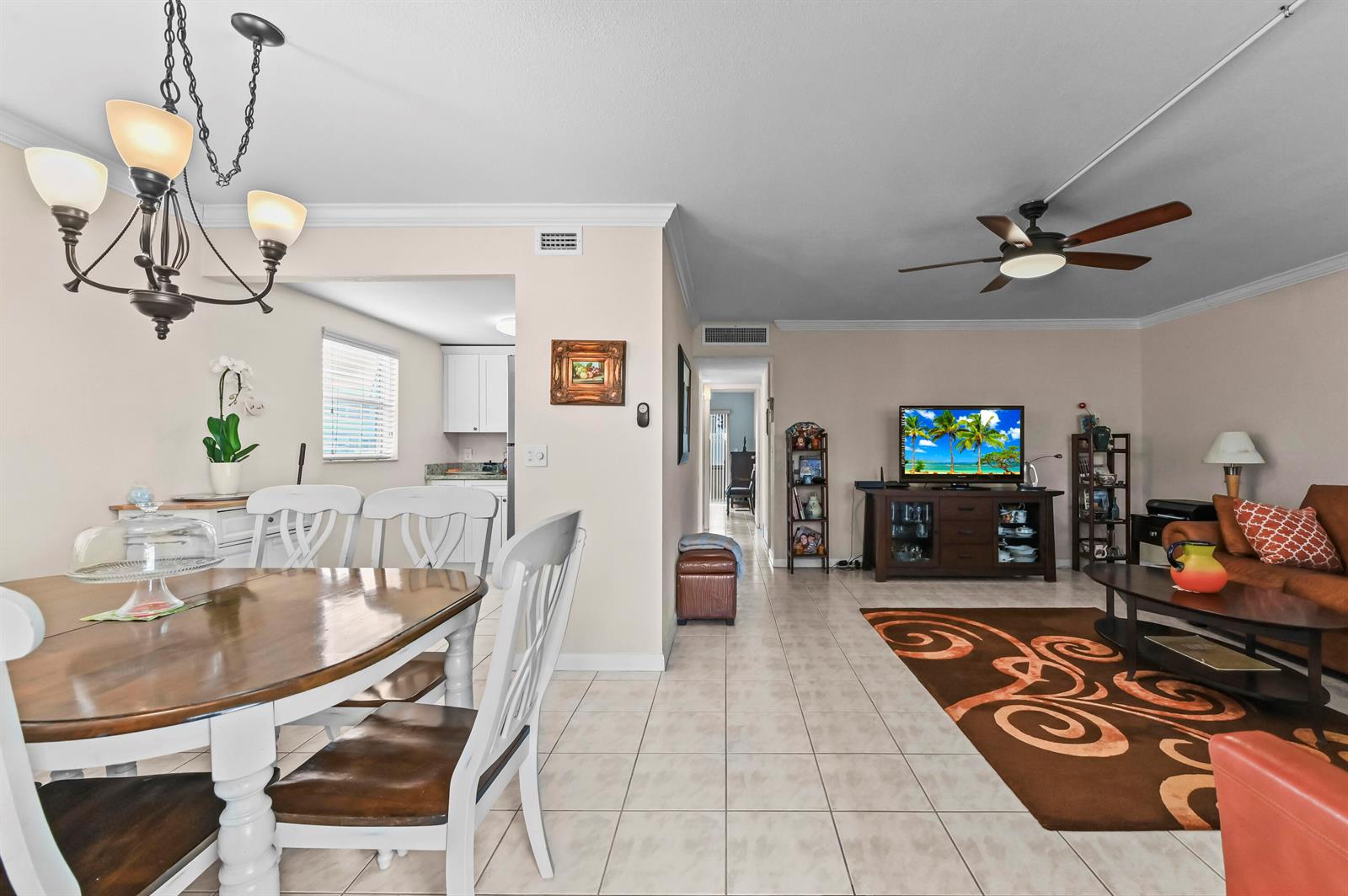 An open-concept living and dining area features tile flooring, a ceiling fan, and white furniture — 213 Brittany, Delray Beach FL 33446, DELRAY BEACH, FL