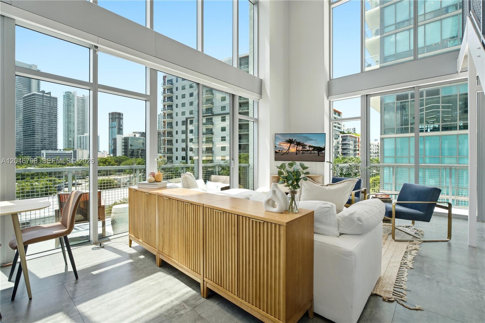 A modern living room features floor-to-ceiling windows, a white sofa, and a wooden console table — 3301 NE 1st Ave, Miami FL 33137, MIAMI, FL