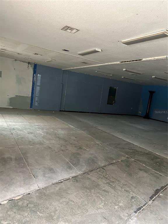 An empty commercial space features blue walls, a drop ceiling, and exposed concrete flooring — 3619 E CR 466, OXFORD, FL