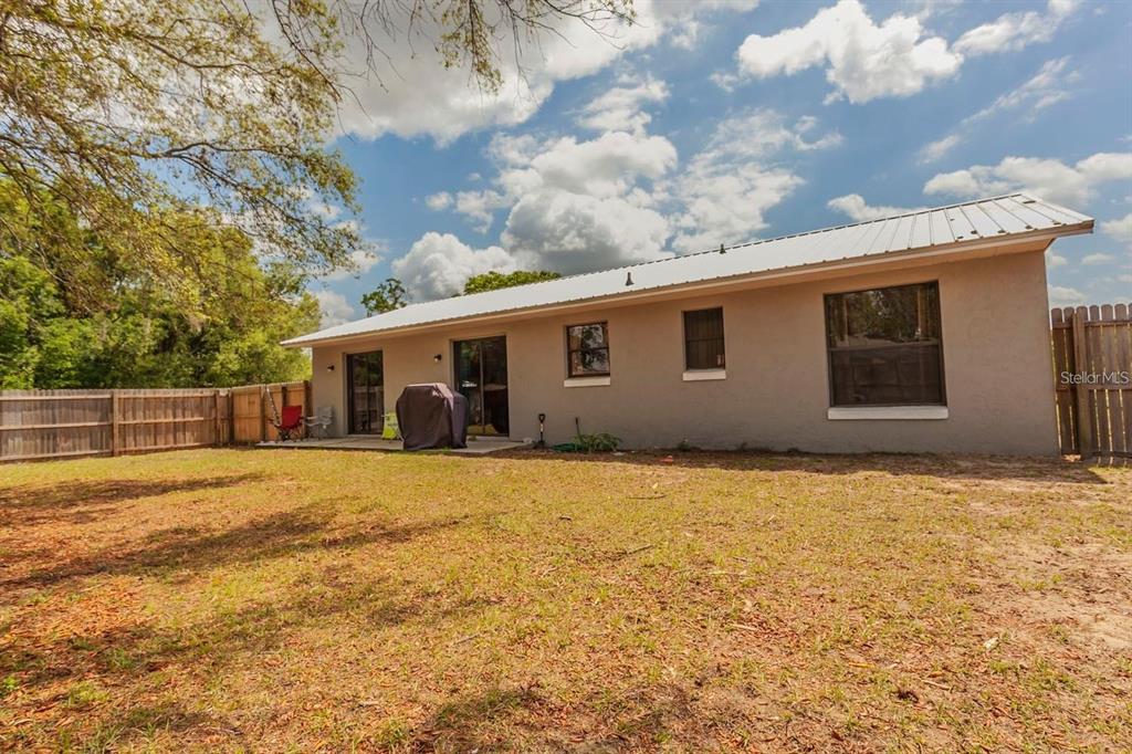 A backyard view of a single-story house with a metal roof and a patio — 7211 SE 120TH STREET, BELLEVIEW, FL