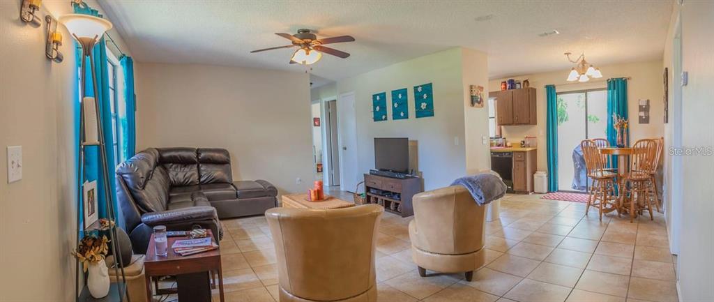 An open-concept living room and dining area features tile flooring, a sectional sofa, and chairs — 7211 SE 120TH STREET, BELLEVIEW, FL