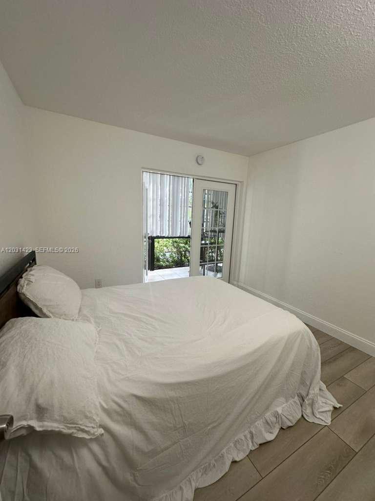 A bedroom features a white bed, light wood-look flooring, and a glass door to a patio — MIAMI, FL