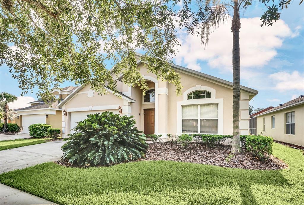 A single-story beige house with a two-car garage, arched entryway, and a palm tree — 153 BAREFOOT BEACH WAY, KISSIMMEE, FL