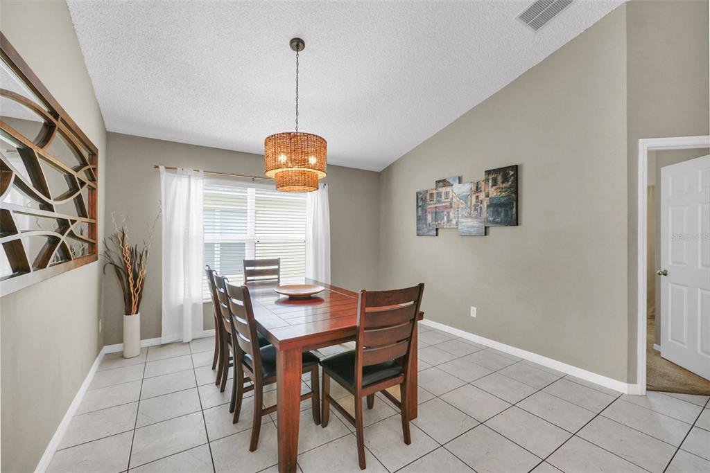 A dining room with a wooden table, chairs, a woven pendant light, and tiled floors — 153 BAREFOOT BEACH WAY, KISSIMMEE, FL