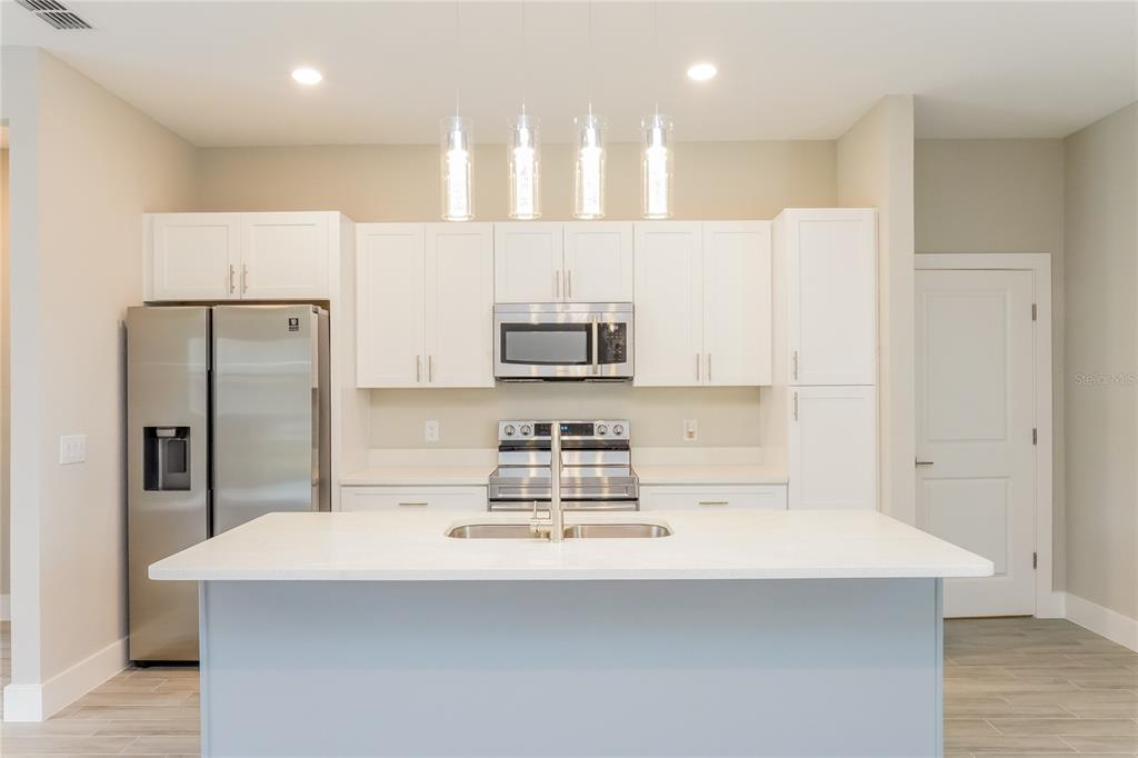 A modern kitchen features white cabinetry, stainless steel appliances, and a large central island — 202 SNAPPER WAY, KISSIMMEE, FL