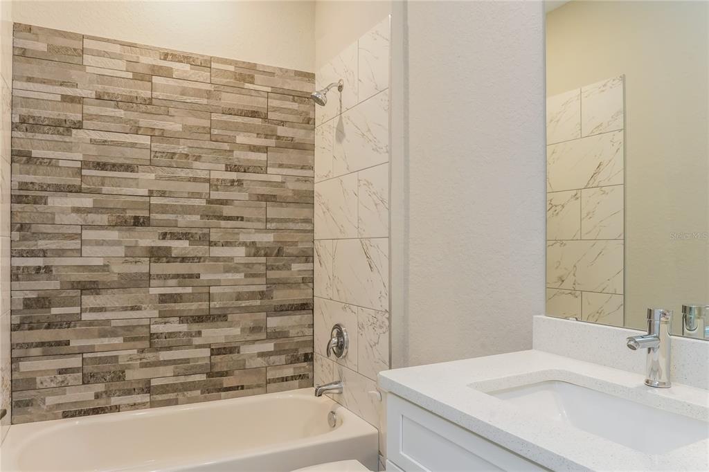 A bathroom features a tub with a stone-look accent wall and white marble-style tile — 202 SNAPPER WAY, KISSIMMEE, FL